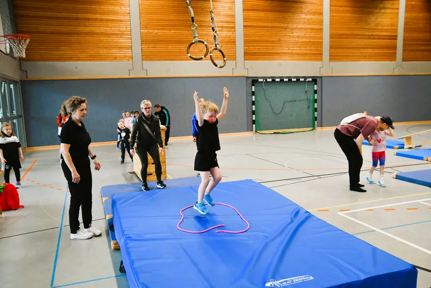 An Ringen schwingend über die Breite zweier Gymnastikmatten schwingen und in einem aufgemalten Kreis auf einem Weichboden im sicheren Stand landen