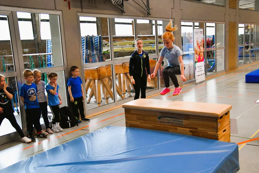 Auf einen 3-teiligen Kasten aufhocken und einen Strecksprung hinunterturnen. 
